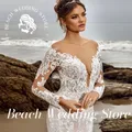 Negozio di matrimoni sulla spiaggia Abito da sposa a sirena con spalle scoperte personalizzato con maniche lunghe in pizzo con scollo a V profondo e ricami floreali intricati